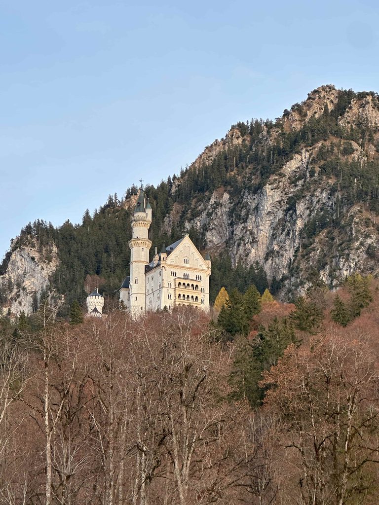 Neuschwanstein Castle peeking out from the trees with mountain in the background